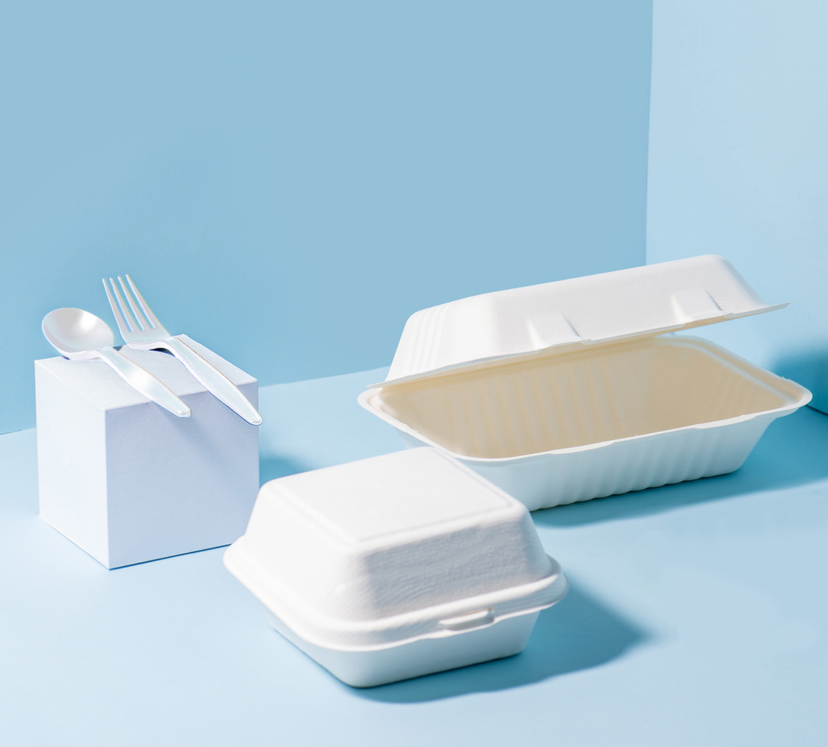 Compostable sugarcane containers and cornstarch cutlery over blue background